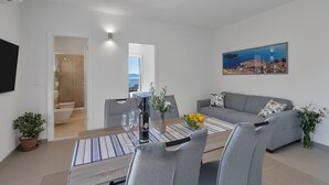 A modern living room with a dining area, grey sofas, a flat-screen TV, and a painting of a cityscape. - Luxury Apartment Podgora-Zora (Podgora)