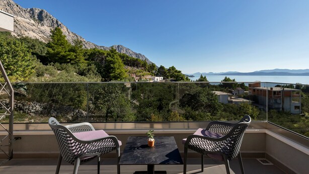A balcony with two chairs and a table, overlooking a mountainous landscape and a body of water. - Luxury Apartment Podgora-Zora (Podgora)