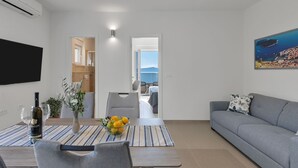 A modern living room with a sofa, a dining table with a vase of flowers, and a TV mounted on the wall. - Luxury Apartment Podgora-Zora (Podgora)