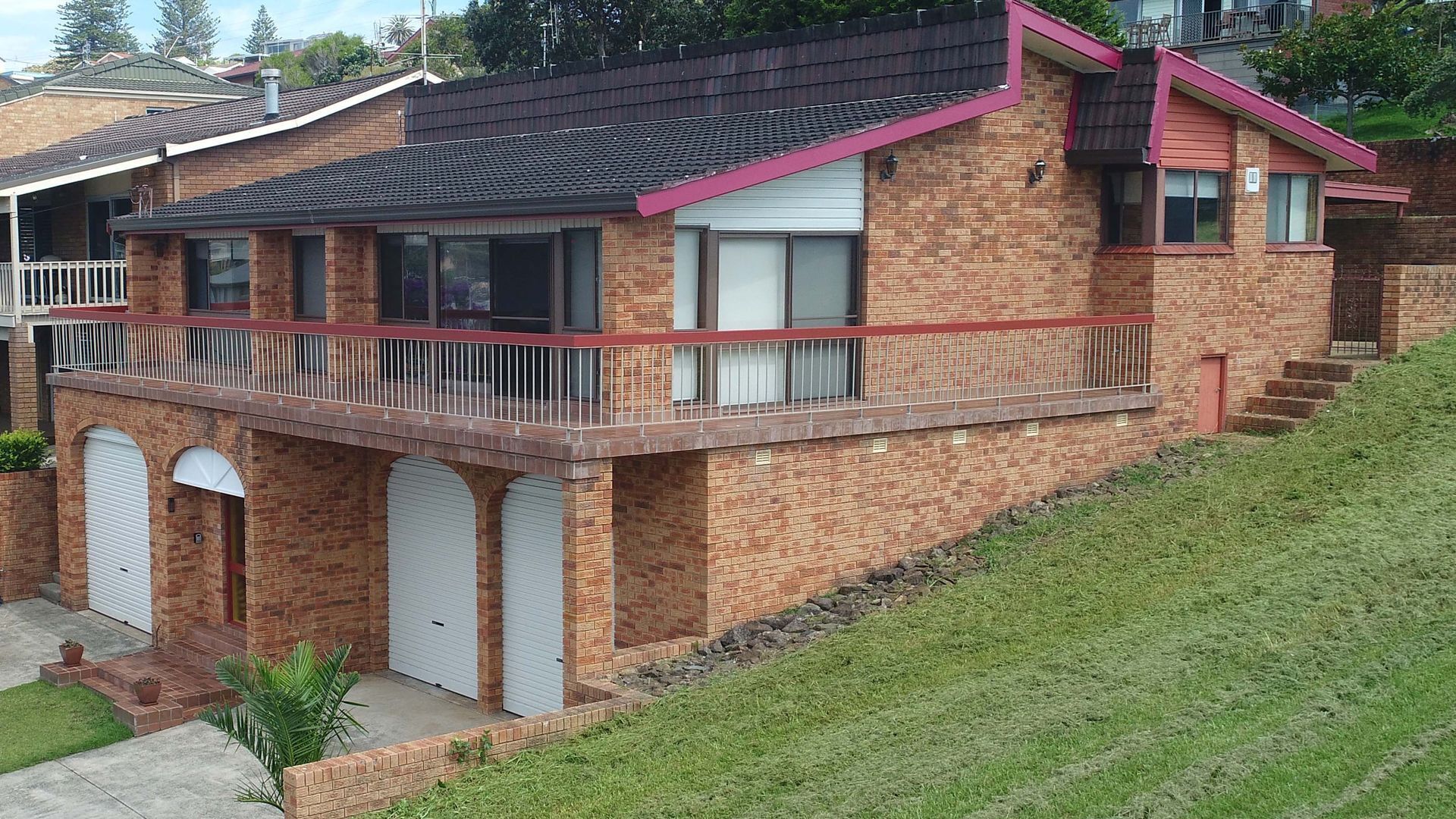 A two-story brick house with a balcony, garage doors, and a small front yard.