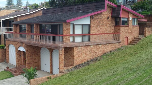 A two-story brick house with a balcony, garage doors, and a small front yard.