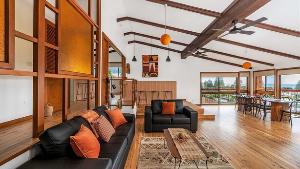 A spacious living area with a black sofa, wooden beams, and a large window offering a view of the outdoors.