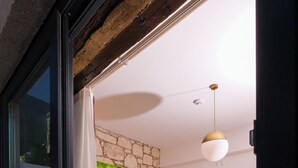 Un dormitorio con pared de piedra, cama con ropa de cama blanca, mesita de noche pequeña y lámpara colgante.