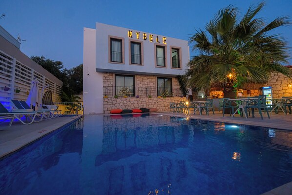 A hotel with a pool, outdoor seating, and a palm tree.