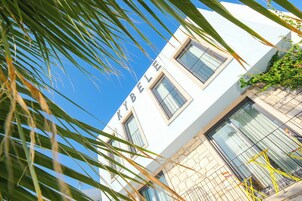 Un edificio blanco con el nombre "BELLE" en la fachada, con múltiples ventanas y un muro de piedra.