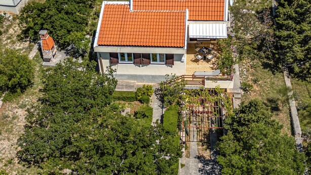 Una casa de dues plantes amb teulada de rajola, un balcó i una zona de jardí.