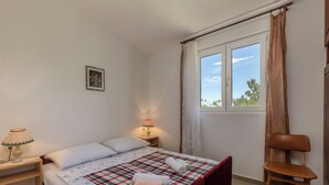 Un dormitori amb un llit, dues làmpades de nit, una cadira, una finestra amb cortines i un quadre petit a la paret.