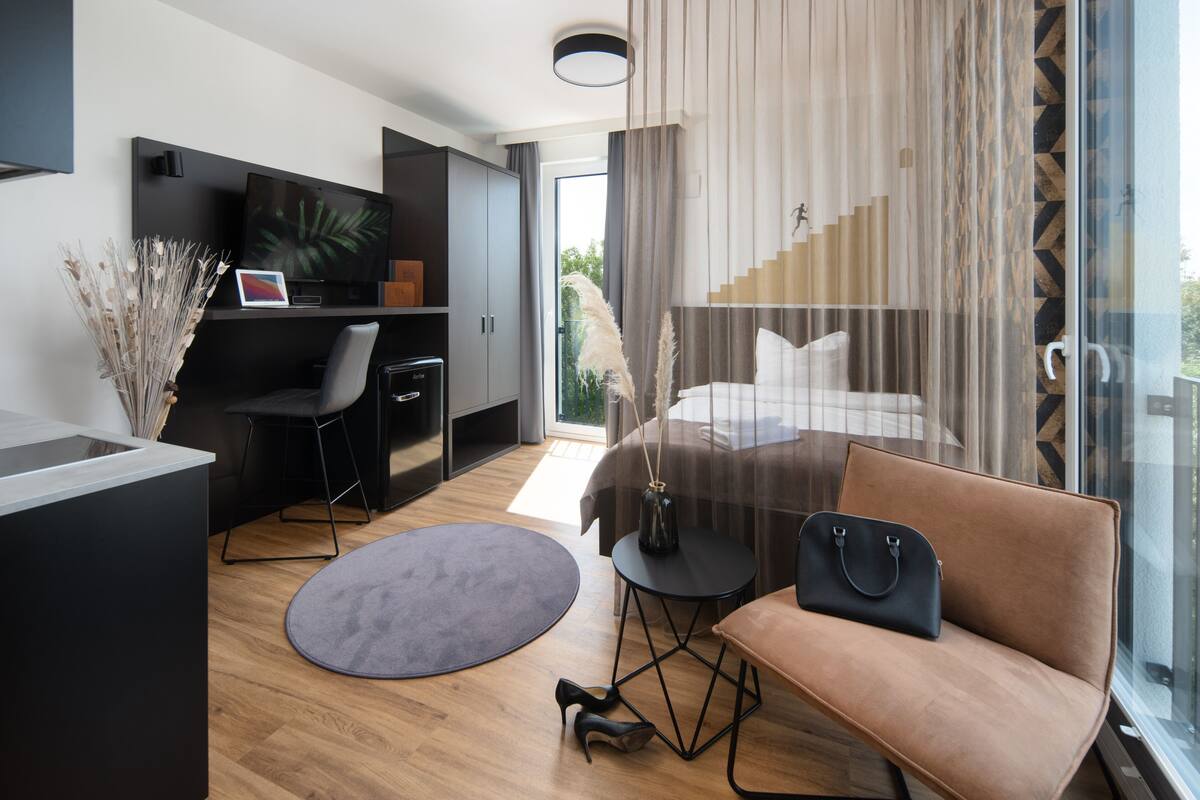 Una habitación de hotel moderna con una cama, un escritorio, una silla, un sofá y un ventanal grande.