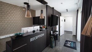 Zona de recepció amb un taulell negre, televisió de pantalla plana i un disseny modern amb il·luminació penjant.