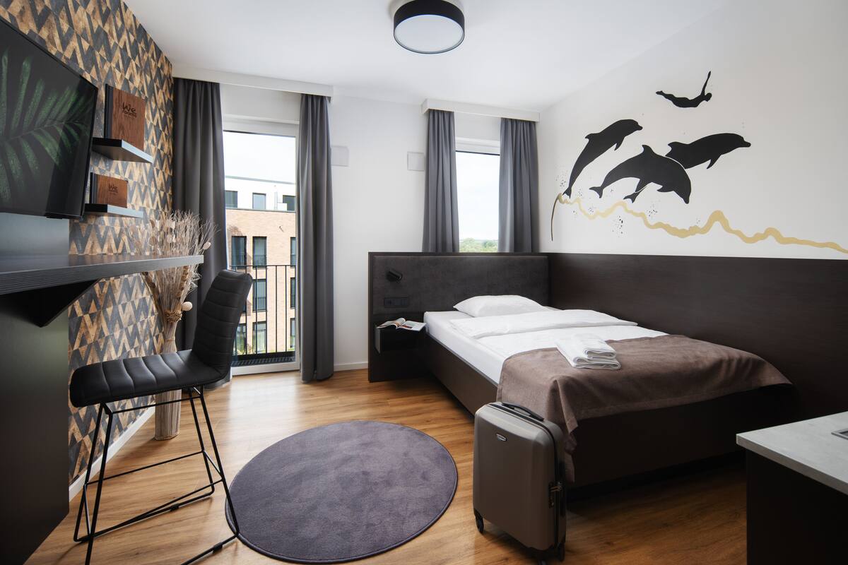 Una habitación de hotel moderna con una cama, un escritorio, una silla, una maleta y un mural de un delfín en la pared.