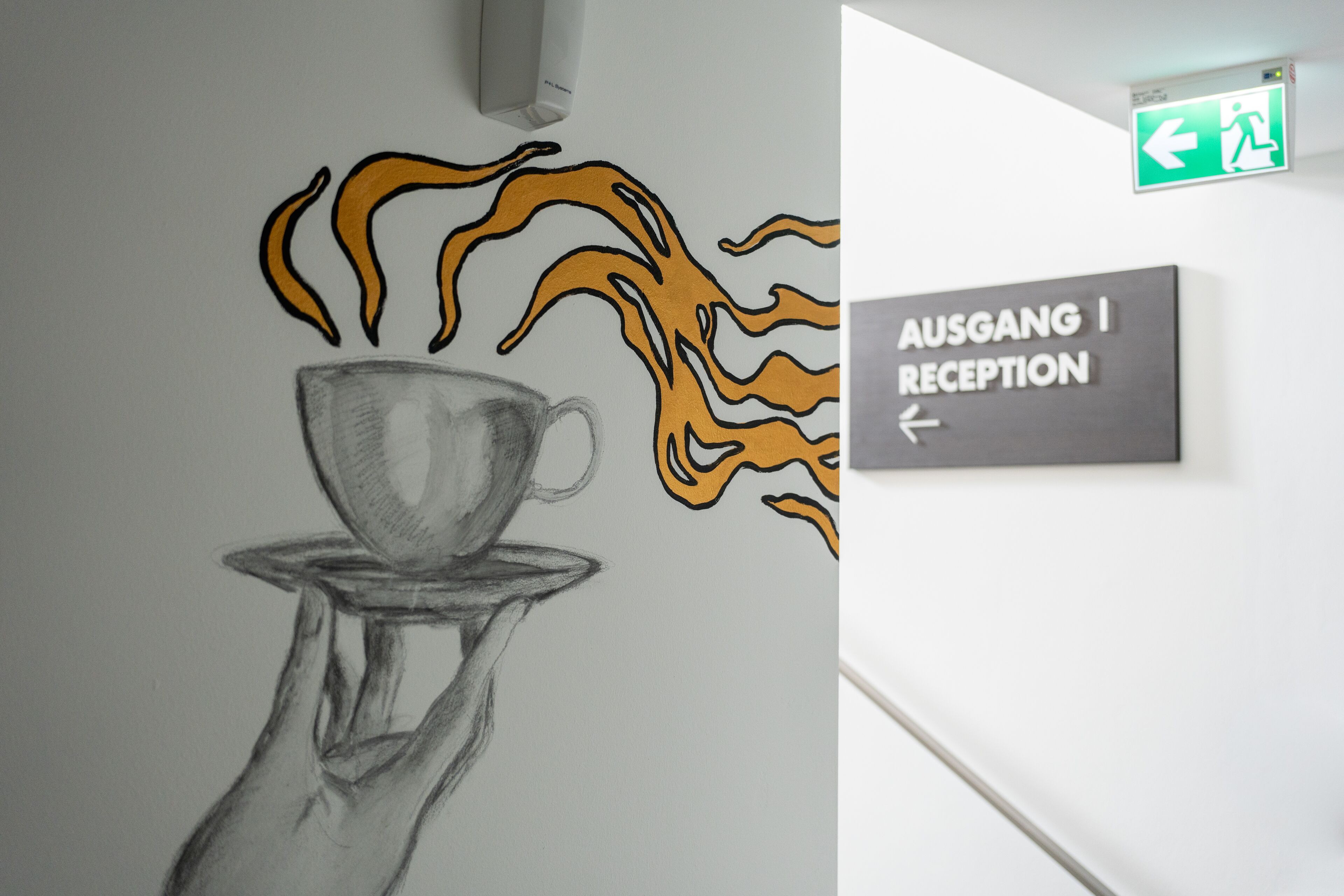A wall with a drawing of a hand holding a cup with flames above it and a sign pointing to the reception.