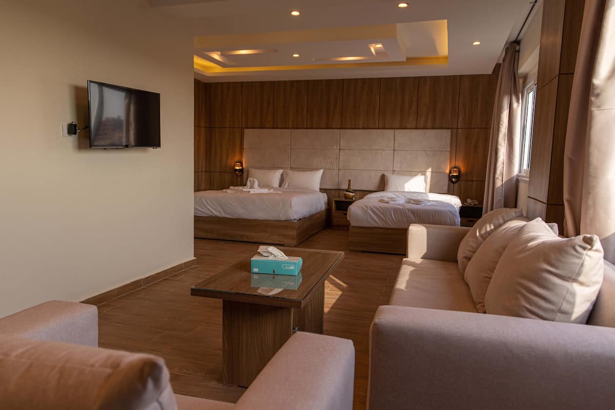 Habitación de hotel con dos camas, un sofá, una mesa de centro y un televisor montado en la pared.