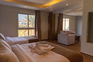 A hotel room with two beds, a sofa, and a large window offering a view of palm trees and buildings. - Nine Pyramids View Hotel (Giza)