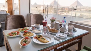A dining table with various dishes, a water bottle, and a view of pyramids. - Nine Pyramids View Hotel (Giza)