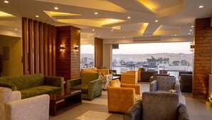 A modern lounge area with sofas and armchairs, a wooden accent wall, and a large window offering a view of the city. - Nine Pyramids View Hotel (Giza)