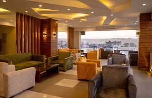 A modern lounge area with sofas and armchairs, a wooden accent wall, and a large window offering a view of the city.