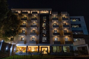 A modern hotel with multiple balconies, a central X-shaped design, and illuminated windows at night. - Nine Pyramids View Hotel (Giza)