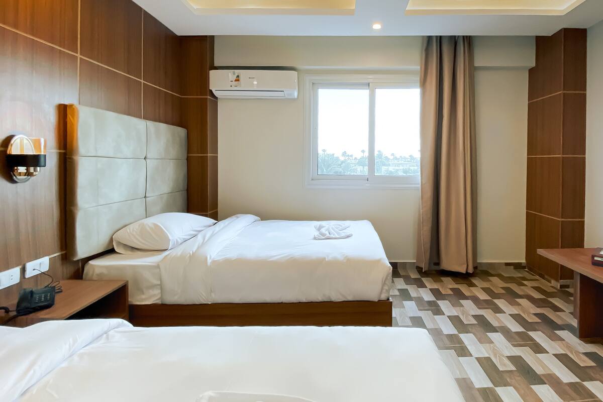 Habitación de hotel con dos camas, ventana con vistas, unidad de aire acondicionado y pared de madera.