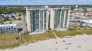 Ein Hochhaus-Hotel mit mehreren Balkonen, einem Schwimmbad und einem Strandbereich mit Sonnenschirmen.