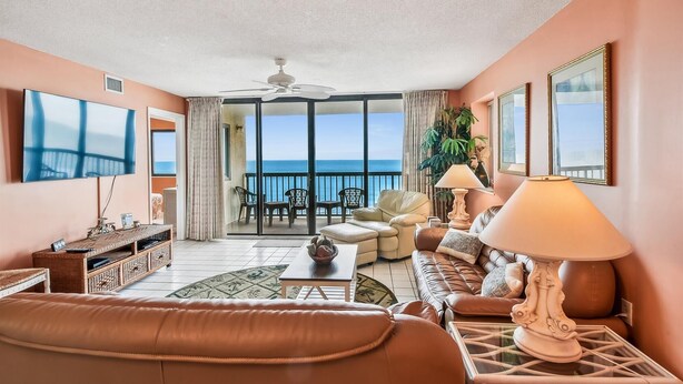 Ein Wohnzimmer mit einer Couch, einem Couchtisch, einem Fernseher und einem Balkon mit Meerblick.