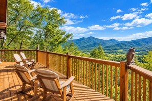 A wooden deck with chairs and a railing overlooking a mountainous landscape.