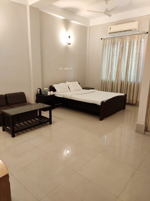 A hotel room with a bed, a sofa, a small table, a ceiling fan, and an air conditioning unit. - Lake Side Resort Neermahal (Sonamura)