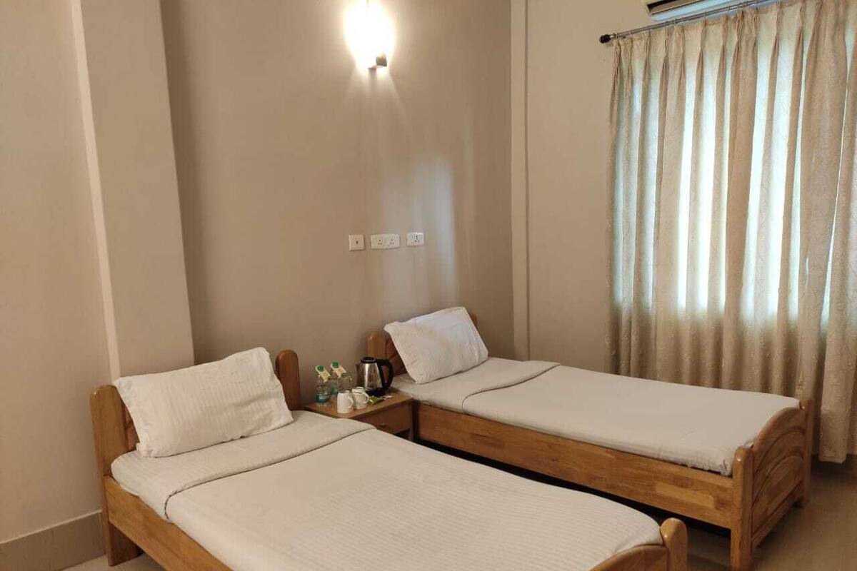 Een kamer met twee houten bedden, een nachtkastje met een lamp en een raam met gordijnen.