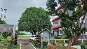 A sign for Polo Lake Resort with a gated entrance, a large tree, and a building with red and grey exterior.