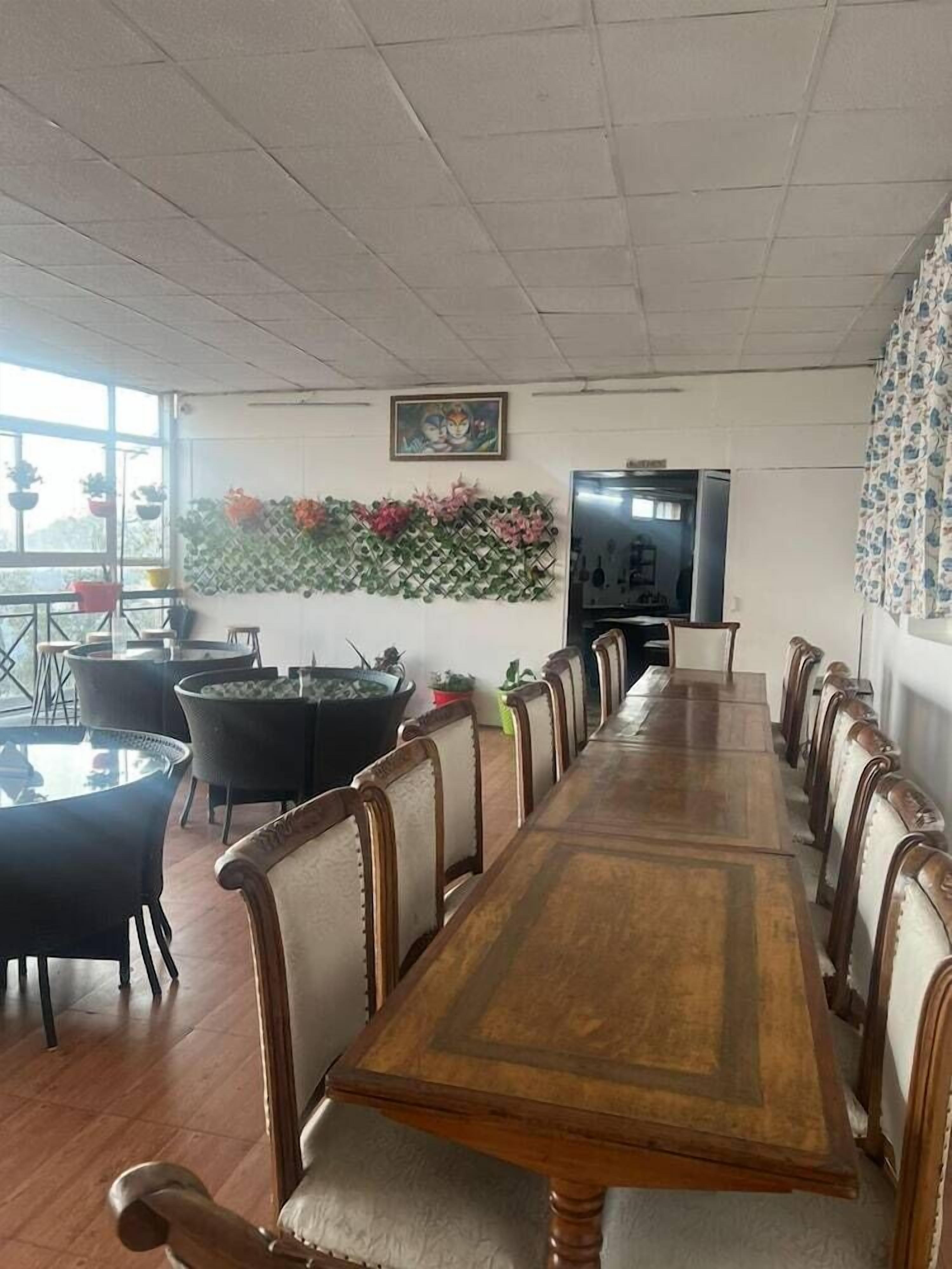 Een vergaderruimte met een lange houten tafel en stoelen, een decoratieve wand met planten, en een televisie.
