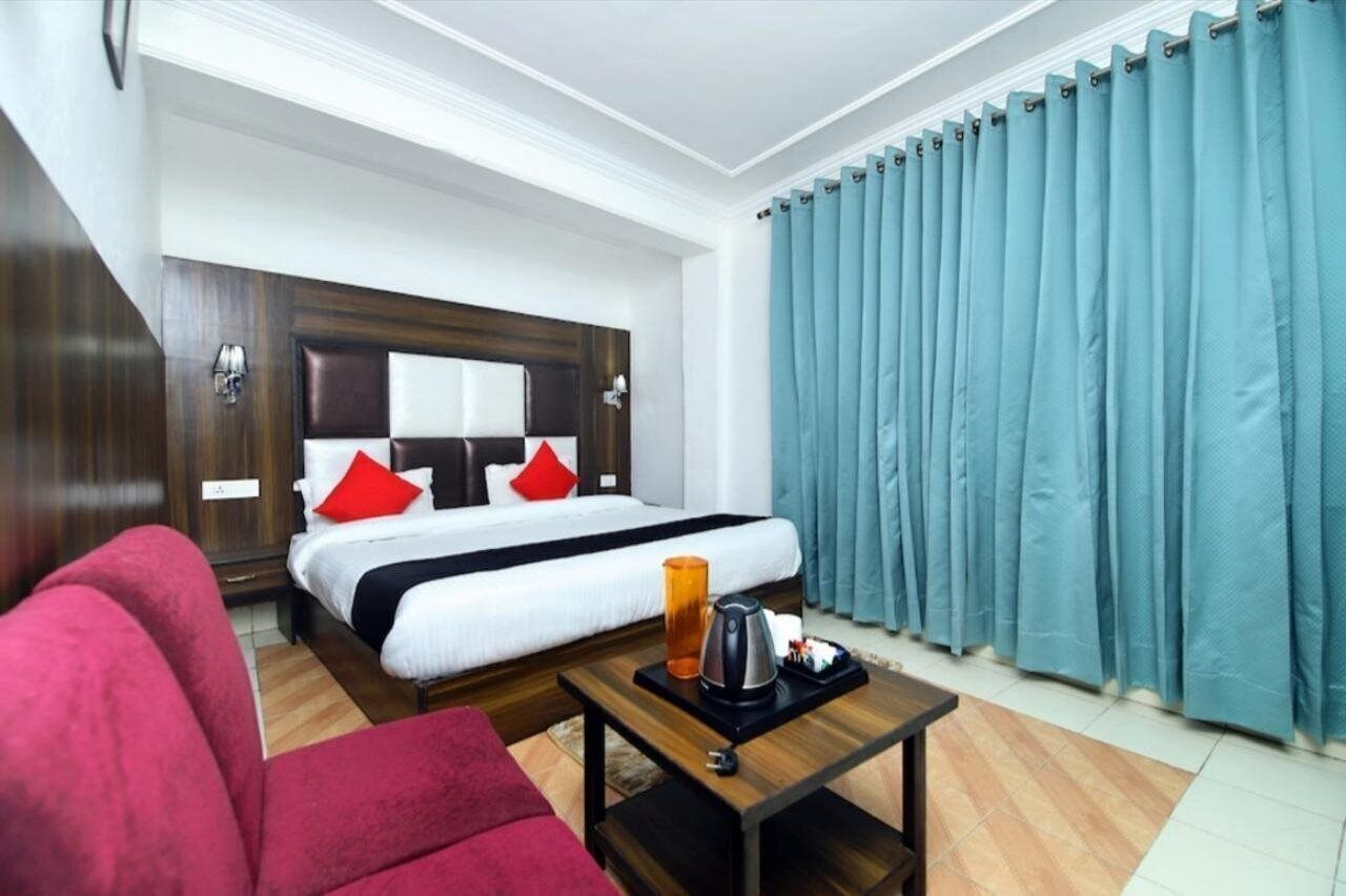A hotel room with a bed, a coffee table, a red sofa, and a large window with curtains.
