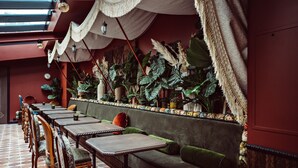 A restaurant with a long dining area, cushioned seating, and large plants. - Babel Belleville (Paris)