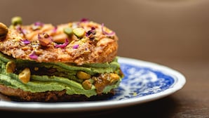 A close-up of a layered pastry with green filling and nuts on a blue and white plate. - Babel Belleville (Paris)