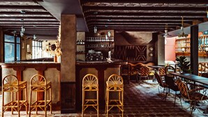 A bar area with wooden chairs, a bar counter, and shelves with bottles. - Babel Belleville (Paris)