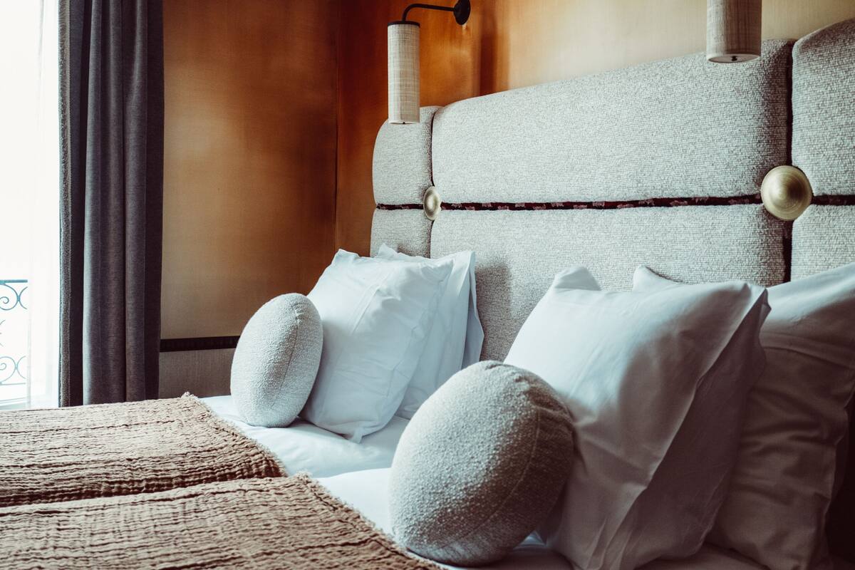A hotel room with a large bed, a headboard with wall-mounted lamps, and a window with curtains.