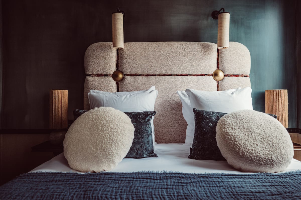 A bed with a textured headboard, white and dark pillows, and a blue blanket.