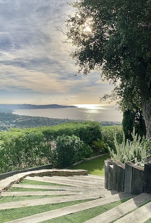 A landscaped garden with a wooden staircase leading to a viewing area overlooking a body of water and distant hills.