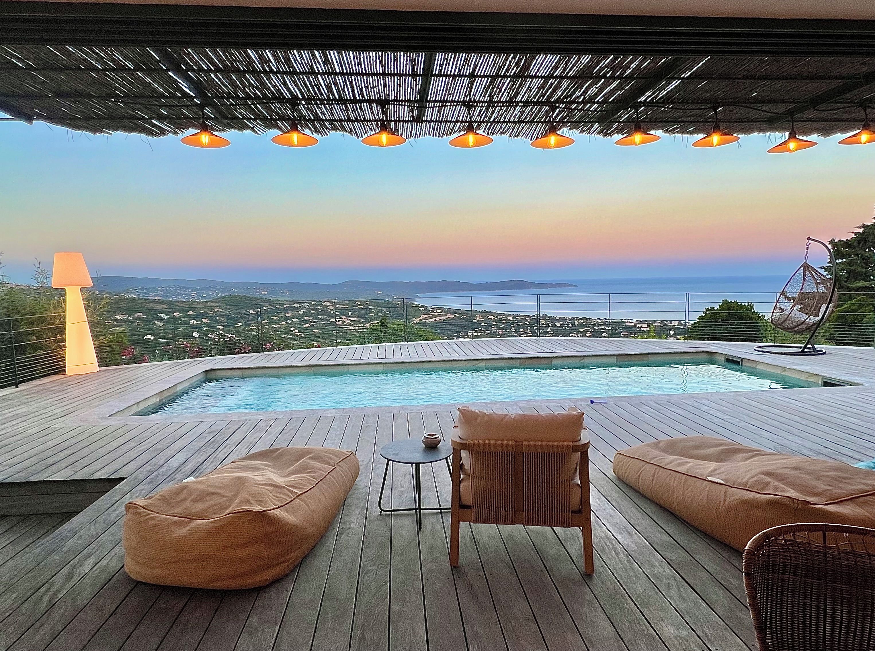 Eine Holzterrasse mit Pool, Sitzgelegenheiten und Meerblick.