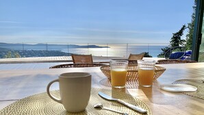 Ein Tisch mit einer weißen Tasse und zwei Gläsern Orangensaft, mit Blick auf eine malerische Meereslandschaft.
