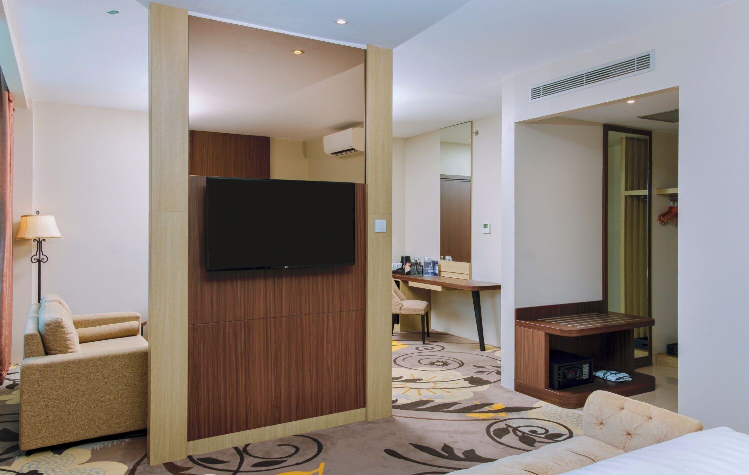 Une chambre d’hôtel équipée d’un téléviseur à écran plat fixé sur un panneau en bois, d’un bureau avec une chaise, d’un canapé et d’un lit.