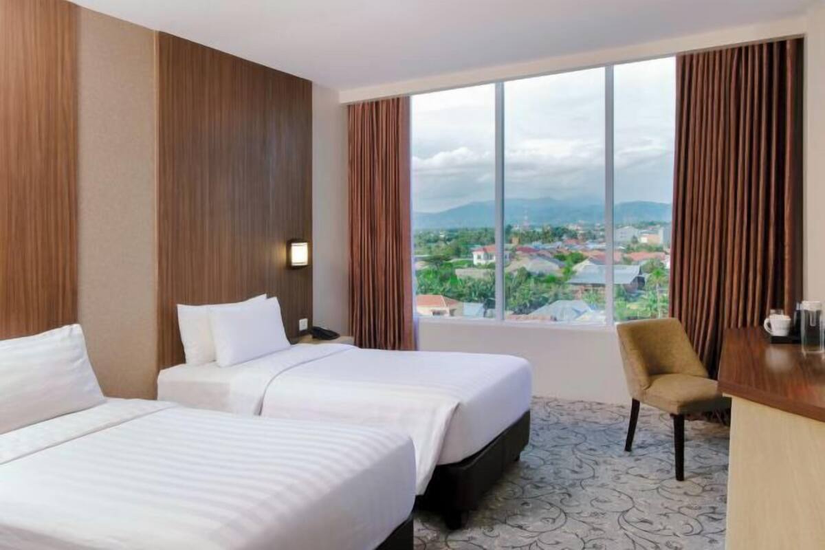 Une chambre d’hôtel avec deux lits, un bureau, une chaise et une grande fenêtre donnant sur la ville.