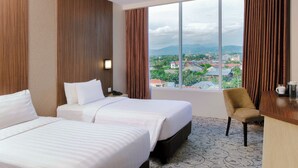 A hotel room with two beds, a desk, and a chair. There is a large window with a view of a cityscape and mountains. - Aston Gorontalo Hotel & Convention Center (Gorontalo)