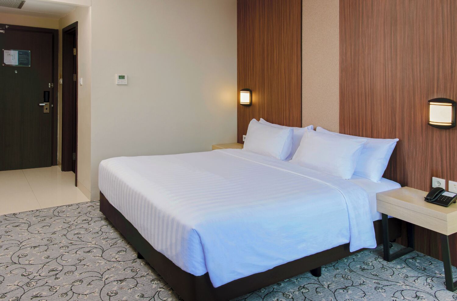 Une chambre d’hôtel avec un grand lit, une table de chevet avec un téléphone et une lampe fixée au mur.