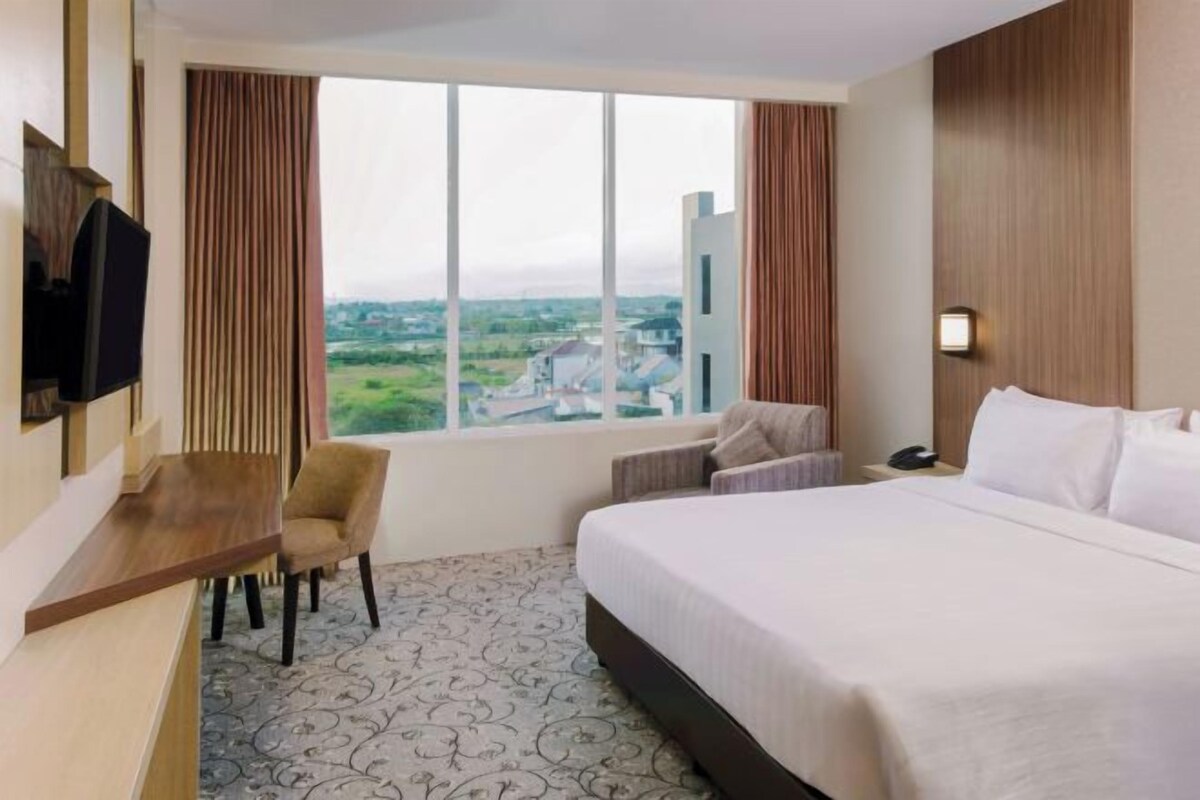 Una habitación de hotel con una cama grande, un escritorio, una silla, un televisor y una ventana con cortinas.