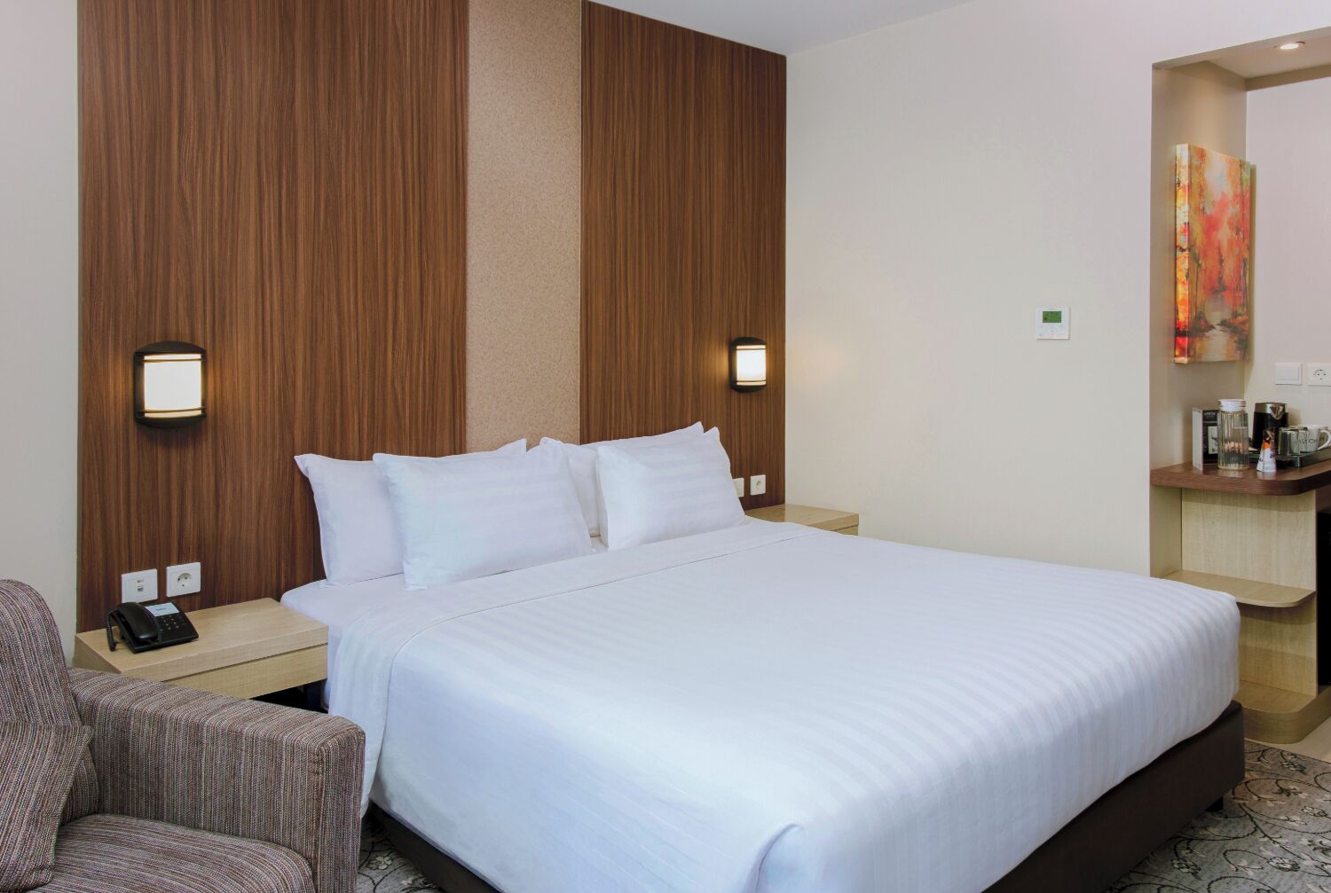 A hotel room with a large bed, two bedside tables with lamps, a chair, and a small desk with a coffee maker.