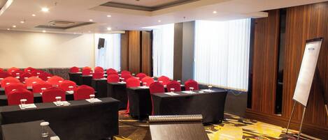 Une salle de conférence avec des rangées de tables, des chaises rouges, un tableau blanc et un sol recouvert de moquette.