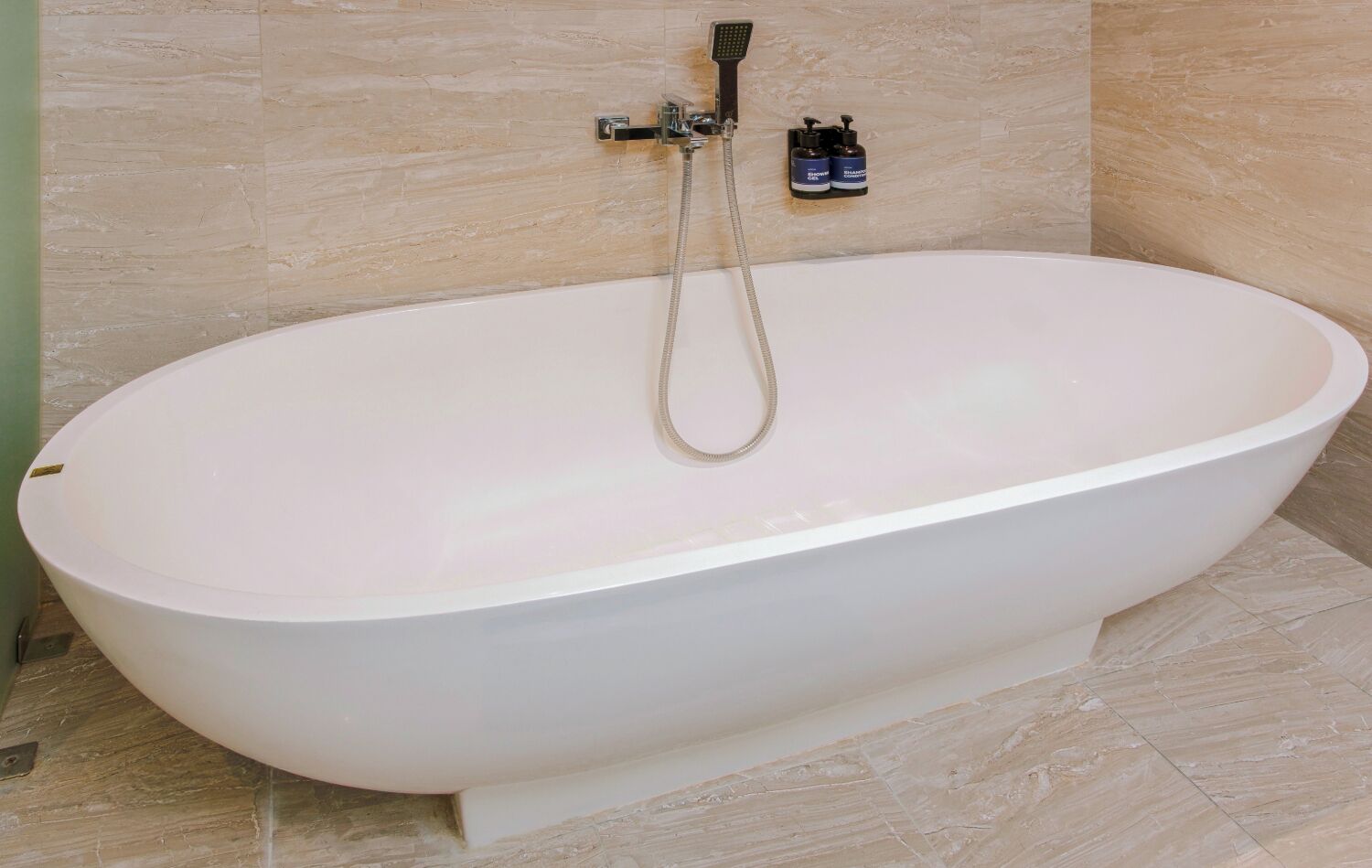 Un baño moderno con una bañera independiente, cabezal de ducha de mano y dos botellas de champú en la pared.