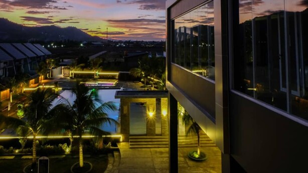 A modern building with a pool and outdoor lighting, surrounded by palm trees and a sunset view. - Aston Gorontalo Hotel & Convention Center (Gorontalo)