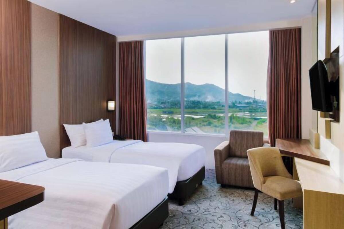 Une chambre d’hôtel avec deux lits, un bureau, une chaise et une grande fenêtre donnant sur les montagnes.
