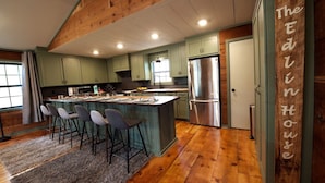 Una cocina con una isla central, taburetes de bar, un refrigerador y una pared de acento de madera con texto.