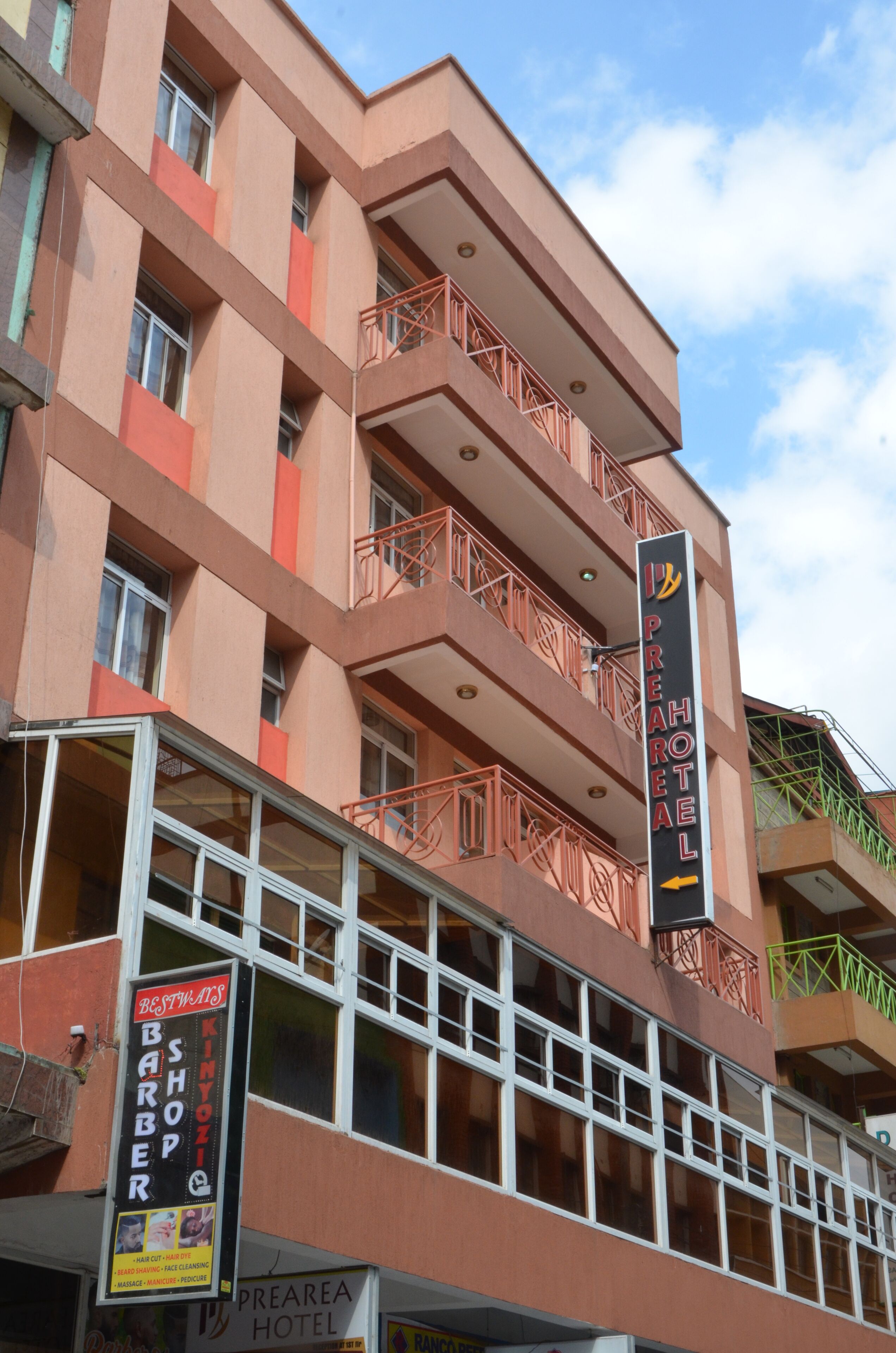 A multi-story hotel with balconies, a sign for a barbershop, and a sign for the Preah Hotel.